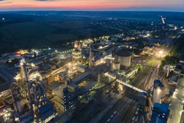 Yüksek beton yapılı çimento fabrikası ve endüstriyel üretim alanında geceleri kule vinçleri. Üretim ve küresel sanayi kavramı.