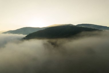 Ufuktaki uzak karanlık dağ siluetleriyle beyaz, yoğun, sisli bulutların üzerinde canlı günbatımının havadan görünüşü..