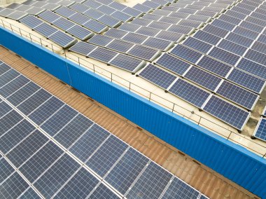 Sanayi binasının çatısına monte edilmiş mavi fotovoltaik panelleri olan güneş enerjisi santralinin hava görüntüsü.