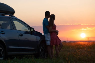 Mutlu çift sıcak yaz akşamında balayı gezileri sırasında SUV arabalarının yanında vakit geçiriyorlar. Genç adam ve kadın doğada arabayla yolculuk etmekten zevk alıyorlar..
