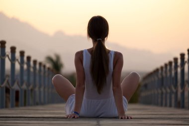 Açık renk elbiseli genç bir kadın deniz kıyısında güneşli bir sabahta dinleniyor. Yaz tatili ve seyahat konsepti.