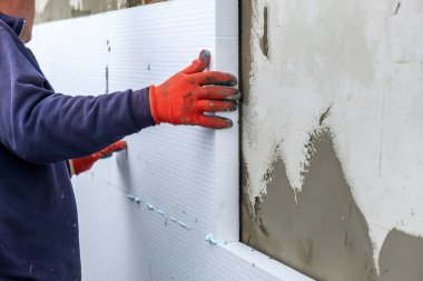 İnşaat işçisi termal koruma için evin ön cephesine köpük yalıtım çarşafları yerleştiriyor..
