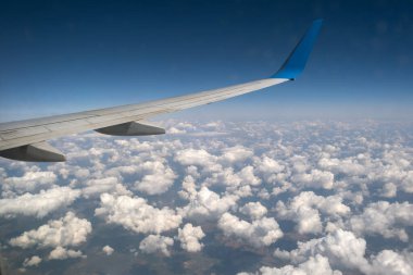 Mavi gökyüzünde beyaz kabarık bulutların üzerinde uçan jet uçağı kanadının görüntüsü. Seyahat ve hava taşımacılığı kavramı.