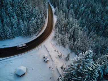 Kış manzaralı, karla kaplı dağ tepeleri ve dolambaçlı orman yolu..