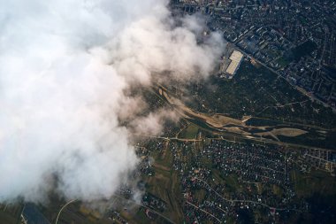 Yükseklerdeki uçak penceresinden, yağmurdan önce oluşan kabarık kümülüs bulutlarıyla kaplı uzak şehrin hava manzarası..