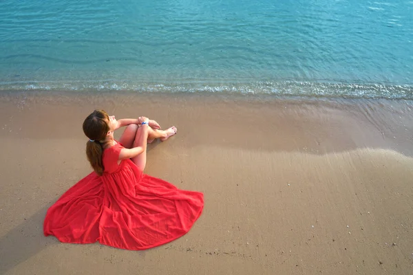 暖かい夏の朝を楽しんで海のビーチで休んで赤いドレスを着て若い幸せな女性 — ストック写真