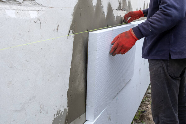 Construction worker installing styrofoam insulation sheets on house facade wall for thermal protection.
