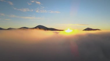 Ufuktaki uzak karanlık dağlarla beyaz yoğun bulutların üzerinde canlı gündoğumunun havadan görüntüsü..