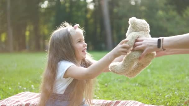 快乐的小女孩坐在夏日公园的绿草上玩她的玩具熊玩具 — 图库视频影像