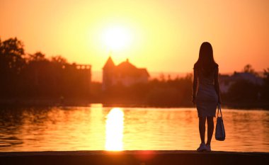 Gölün kıyısında tek başına duran ve sıcak akşamın tadını çıkaran yalnız bir genç kadın. Doğada refah ve rahatlama kavramı.