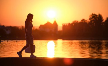 Yalnız genç bir kadın göl kıyısında yalnız yürüyor sıcak akşamın tadını çıkarıyor. Doğada refah ve rahatlama kavramı.