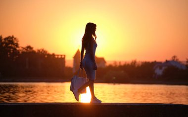 Sıcak bir akşamda göl kenarında yalnız başına yürüyen yalnız bir yaya kadın. Yalnızlık ve rahatlama kavramı.