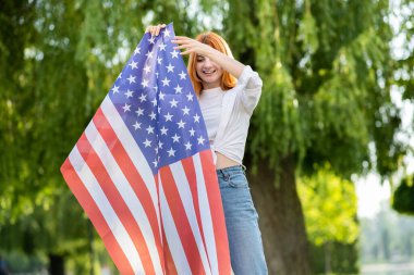Yaz parkında Amerikan bayrağıyla poz veren mutlu genç kız. Açık havada afişi olan pozitif genç bir kadın..