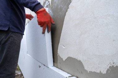 İnşaat işçisi termal koruma için evin ön cephesine köpük yalıtım çarşafları yerleştiriyor..