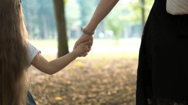 Annemin ve küçük kızının yaz parkında el ele yürürken görüntüsü..
