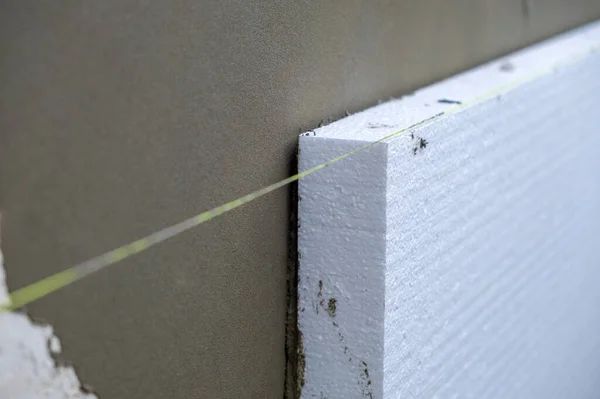 Installation of styrofoam insulation sheets on house facade wall for thermal protection.