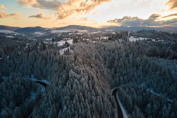 雪に覆われた山の丘や朝の曲がりくねった森の道と冬の風景の空中ビュー — ストック写真