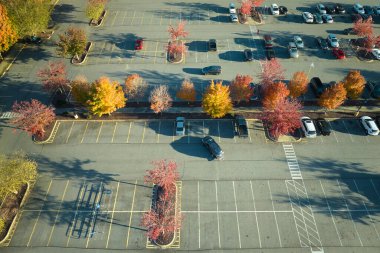 Aerial view of large parking lot with many parked colorful cars. Carpark at supercenter shopping mall with lines and markings for vehicle places and directions.
