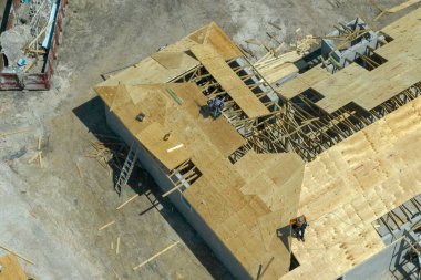 Florida 'nın banliyö bölgesinde inşaat halindeki ahşap çatı iskeleti yapısı olan bitmemiş bir ev üzerinde çalışan inşaatçıların hava görüntüsü..