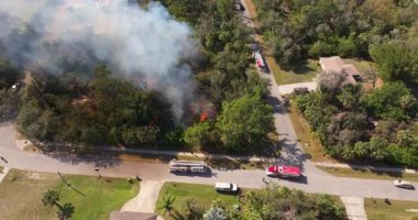 Florida civarındaki evlere tehlikeli bir şekilde yakın yanan bitki örtüsü yangınına müdahale eden itfaiyeciler ve itfaiye araçları görülüyor..