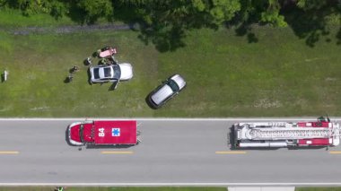 Vehicle collision with emergency technicians assisting victim on stretcher, surrounded by first responders and rescue staff