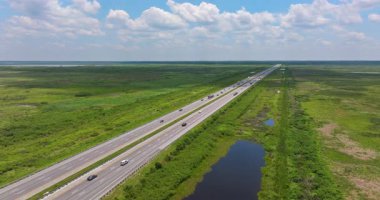 Güneşli bir günde hareket halindeki araçlarla bataklık ve sulak alanlarla çevrili Florida kırsalının hava manzarası.