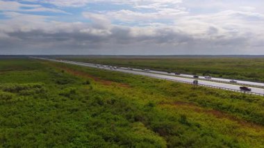 Florida otoyolunun hava manzarası mavi gökyüzünün altında hareket eden araçlarla doğal sulak araziyi kesiyor.