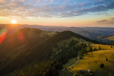 İnanılmaz bir dağ manzarası. Sarı batan güneşle aydınlatılmış koyu ladin ormanları. Vahşi ulusal park dağlarında parlak renkli gün batımı.