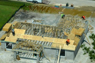 Florida 'nın banliyö bölgesinde ahşap iskeleti olan bitmemiş bir konutun çatı inşaatında çalışan inşaatçılar. Konut geliştirme kavramı.