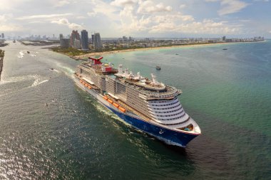Büyük yolcu gemisi gün batımında Miami limanından ayrılıyor. Yüksek binalı otelleri ve konut kuleleri olan South Beach sahil manzaralı.