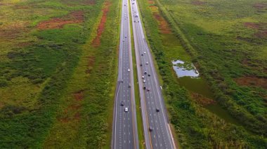 Güneşli bir günde hareket halindeki araçlarla bataklık ve sulak alanlarla çevrili Florida kırsalının hava manzarası.