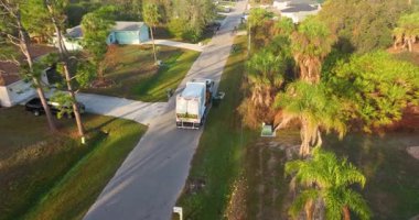 Sanitation truck lifts garbage bins from the curb in quiet suburban neighborhood, providing routine waste collection service in Florida town.