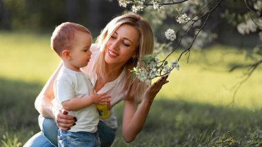 Anne çocuğa çiçek açan bir ağacın dalını gösterir.