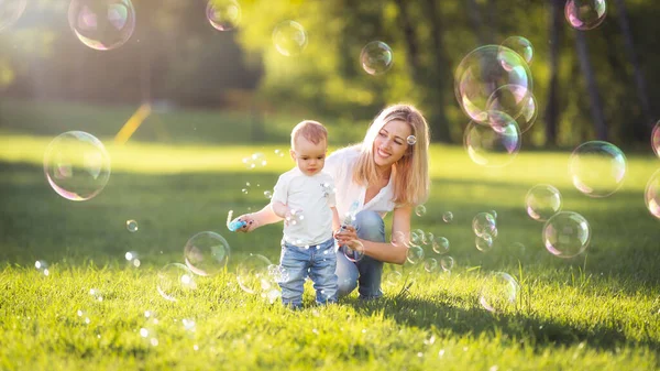 Mamá y bebé soplan burbujas en el parque — Foto de Stock