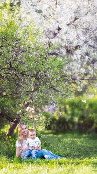 Mamá y el niño están sentados en el césped bajo un árbol floreciente en la naturaleza — Foto de Stock
