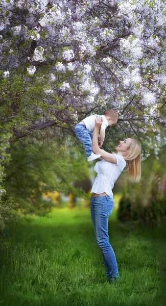 Mamá levantó al bebé en sus brazos cerca de un árbol en flor en primavera — Foto de Stock