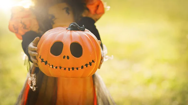 Pompoen hoofd Jack-o-lantaarn in de handen van een meisje in een heks kostuum op straat met een kopieerruimte, achtergrond voor Halloween — Stockfoto