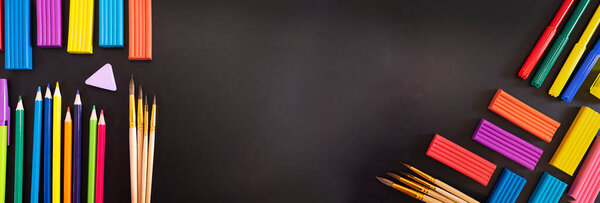 Everything for creativity, various stationery on a black background of a chalk board with copy space: scissors, felt-tip pens, plasticine, pens, pencils, ruler, eraser, sharpener