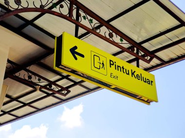 Canlı sarı bir işaret, korunaklı bir gölgelik altında ok ve resimli bir çıkış olduğunu gösteriyor..