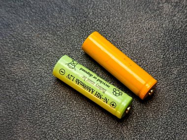 Yeşil ve turuncu bir pil, zıt renklerde, dokulu gri bir yüzey üzerinde çapraz olarak yatıyordu..