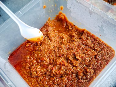 İştah açıcı kırmızı biber ezmesiyle dolu bir kap, servis için beyaz bir plastik kaşık ile gösteriliyor..