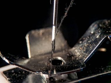 Siyaha karşı metalik bir yüzey üzerinde sergilenen iplikli bir iğne dikiş projeleri için hazırdır.