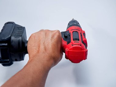 Kırmızı ve siyah kablosuz matkap beyaz arka planda bir insan elinde tutulur..