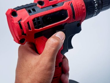 Birisi, matkabın sapına odaklanarak beyaz zemine karşı kırmızı ve siyah bir matkap tutuyor..