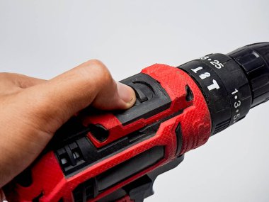 Bir el, kırmızı tutuş ile kablosuz matkabın tetiğine basar, aracın tasarımını gösterir.