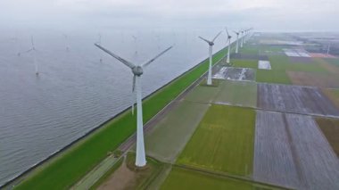 Kıyı boyunca türbinleri olan ve bulutlu bir günde denizde bulunan büyük bir rüzgar çiftliğinin havadan görüntüsü.