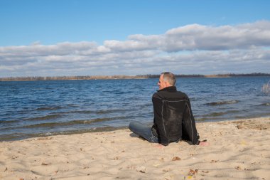 Hiker man sitting on the beach, back to camera, smiling, relaxin