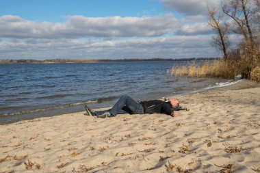 Hiker man relaxing on the beach, lying on the sand, smiling look