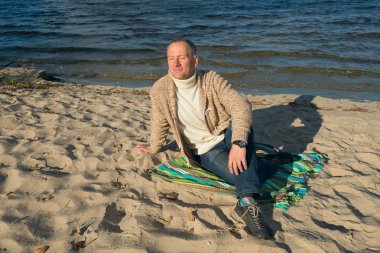 Neşeli gülümseyen adam, rahat giyen, sahilde oturan, looki