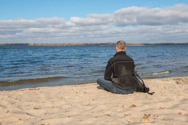 Hiker man sitting on the beach, back to camera, relaxing, thinki